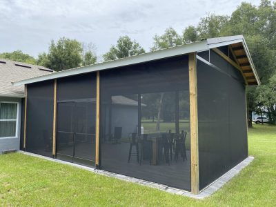 Backyard screened-in porch with black mesh walls, wooden posts, and seating inside the enclosure