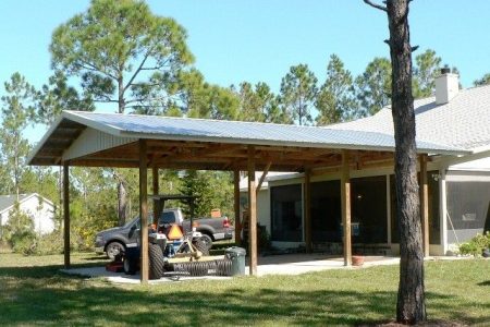 A single-story house with a metal-roofed covered patio; a tractor and other lawn equipment sit under the shelter in front of the home.