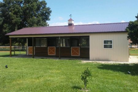 Small horse stable with a purple roof and three front stalls in a grassy field.