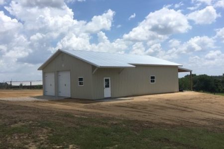 Metal storage building on a bare dirt lot under a partly cloudy sky.