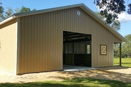 Beige metal storage building with a wide open front bay in a park setting, a small square window on the side, and a dirt path leading inside, under a blue sky.
