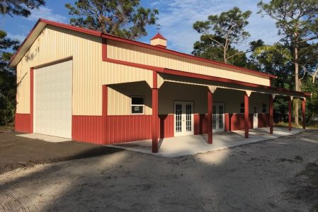 Beige and red metal building with a large white garage door on the left and a covered porch along the front with several doors.