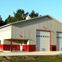 Metal utility building with two large white bay doors, red trim, and a small porch area with picnic tables in front.