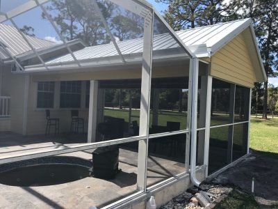 Screened-in patio enclosure attached to a yellow house, with a hot tub and outdoor seating visible inside.