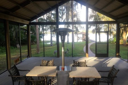 Screened porch with metal patio furniture facing a grassy yard and a lake, surrounded by moss-draped trees and a stone path on the right.