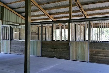 Interior of a horse barn with stalls along a concrete floor and wooden panels under a metal roof.