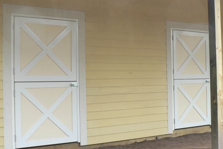 Yellow wooden wall with two white barn doors, each featuring an X-shaped cross and metal latches.