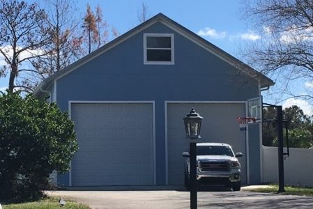 Blue two-car garage with white trim and a small upper window, driveway with a white pickup truck, street lamp in front yard, and a basketball hoop on the right side.