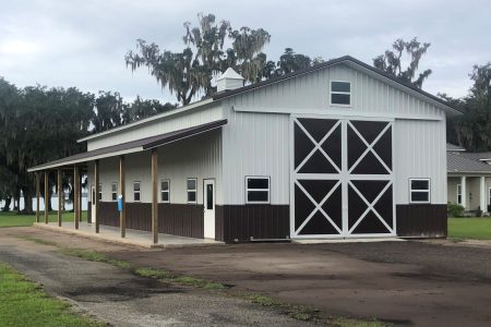 White barn-style building with large black doors cross-braced by white X patterns, under a cloudy sky.